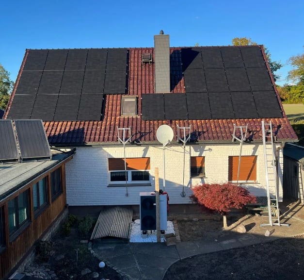 Wohnhaus mit vollflächig belegtem Photovoltaikdach und einem Außengerät im Hof