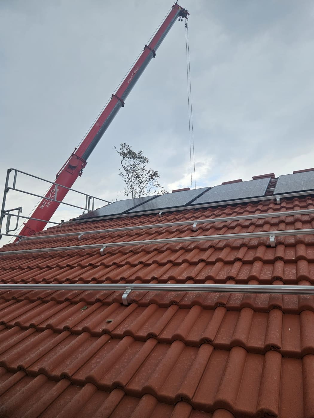 Autokran neben einem Wohnhaus hebt Montagematerial auf das Dach