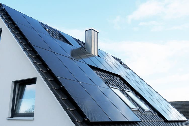 Schwarze Photovoltaikmodule auf einem Ziegeldach vor blauem Himmel
